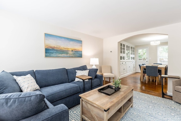 A living room with a sofa, coffee table, and a painting of a sunset over water.