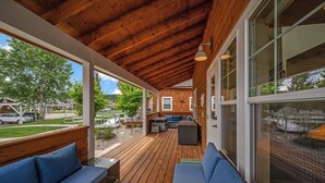 Un espace extérieur abrité doté d’un plancher en bois, de sièges bleus et de grandes fenêtres.