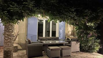 Ein Terrassenbereich im Freien mit Korbmöbeln, einem Tisch mit Glasplatte und einem Steinboden.
