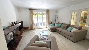 A living room with a sofa, a coffee table, a fireplace, and a view through a glass door. - VILLA FOR 6 PEOPLE, PRIVATE POOL, NEAR BEACH, SAINTE-MAXIME (STE MAXIME)
