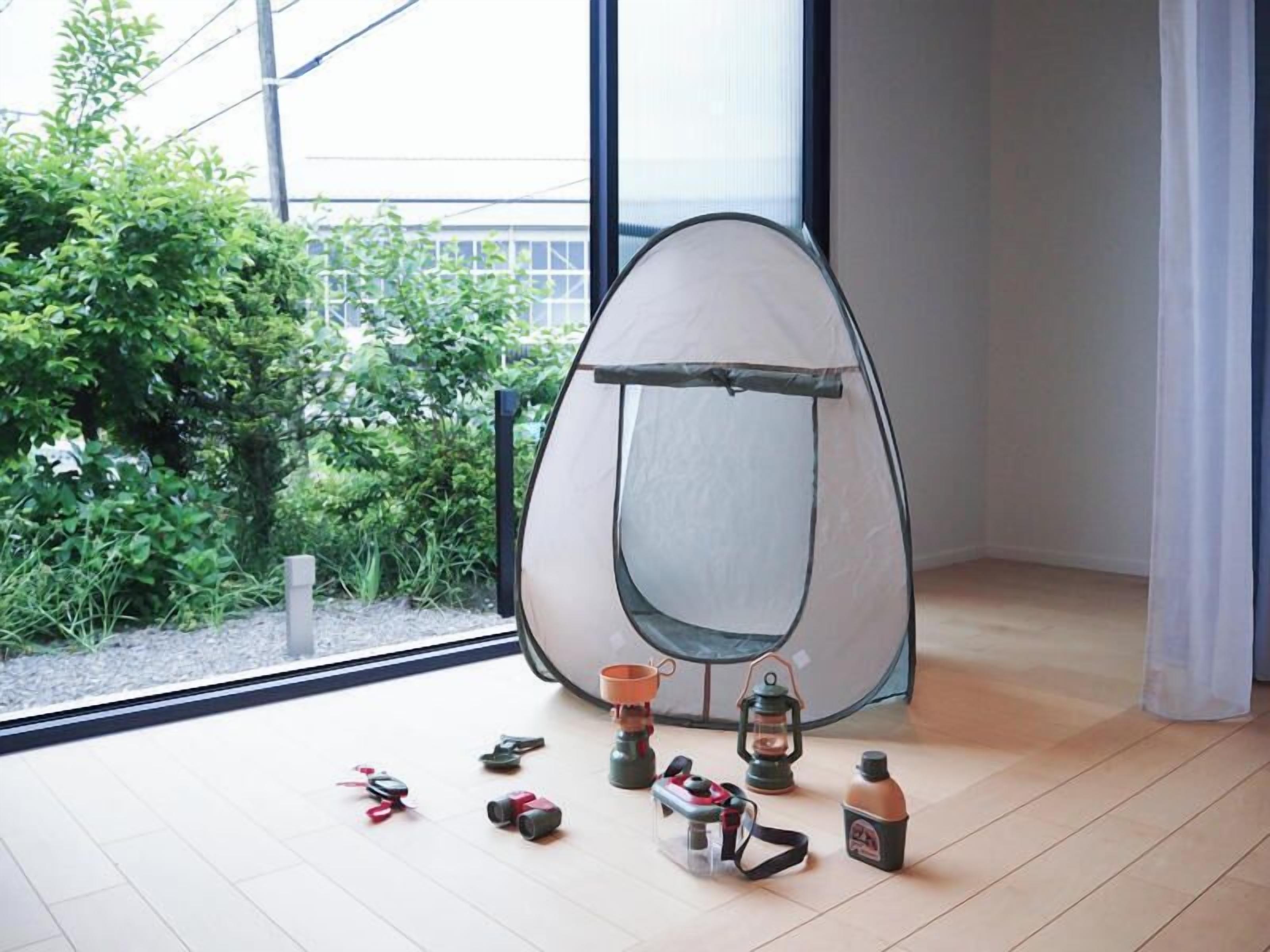A room with a large window, a tent-like structure, and various camping items on the floor.