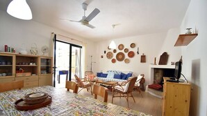 A room with a dining table, chairs, a sofa, a television, and a fireplace. - Casa Vacanze Il Bouganville (Chia)