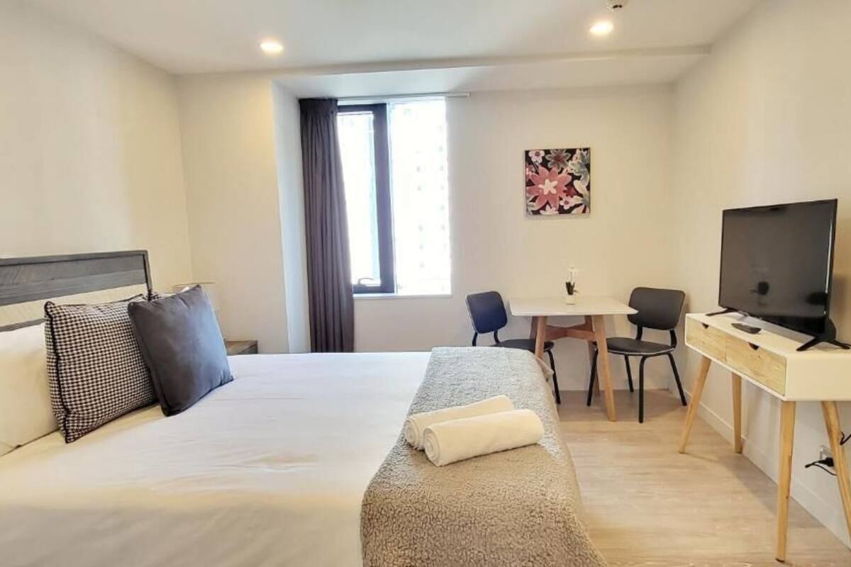 A hotel room with a bed, a desk, a chair, a TV, and a window.