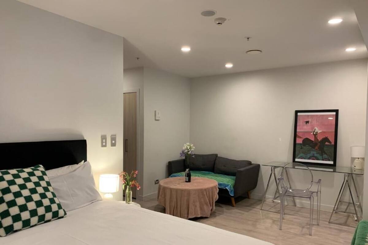A modern hotel room with a large bed, a small round table with a vase of flowers, a sofa, and a TV on a stand.