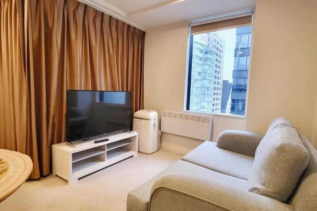 A living room with a flat-screen TV, a white sofa, and a window with a view of buildings.