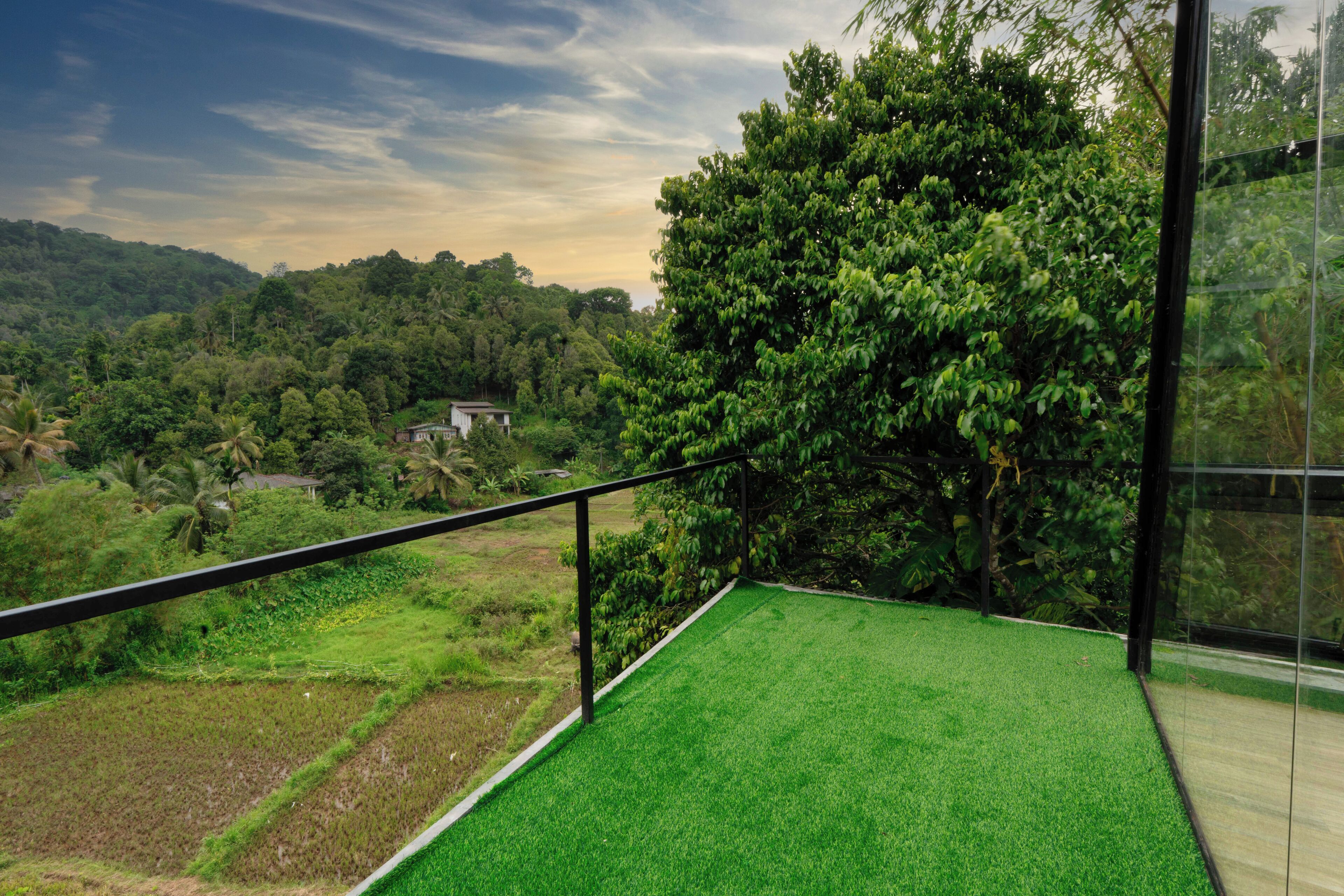 A balcony with a view of a lush green landscape, including trees and a distant building.