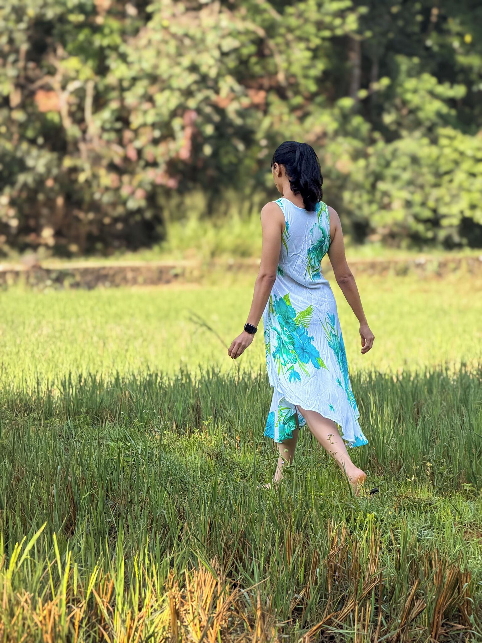 A person walking in a grassy field with trees in the background.