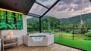 A modern bathroom with a glass-enclosed jacuzzi, wooden flooring, and a large window offering a view of a lush green landscape. - The Blackberry Retreat Kandy (Kandy)