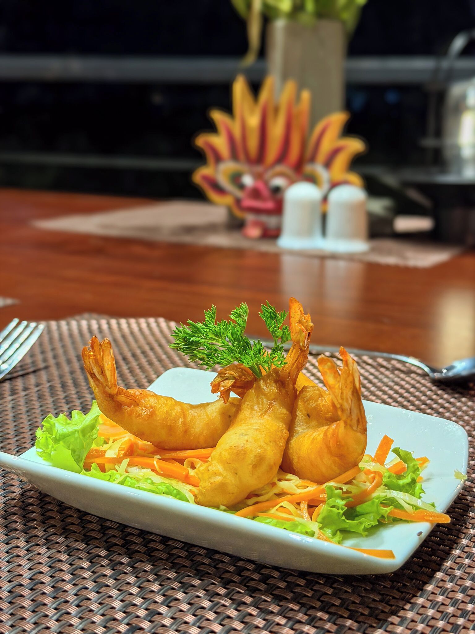 Un plato de camarones fritos con lechuga y zanahorias sobre un camino de mesa tejido.
