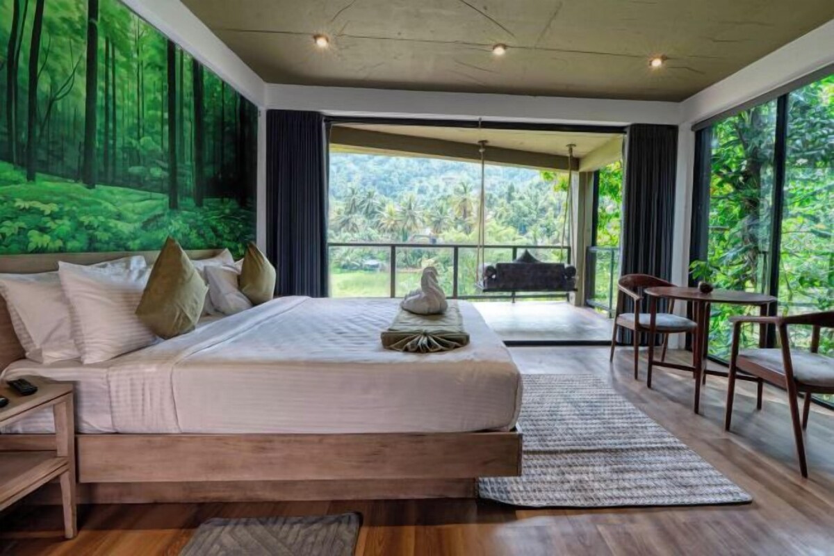A bedroom with a large bed, a nightstand, a chair, and a view of the outdoors through a glass door.