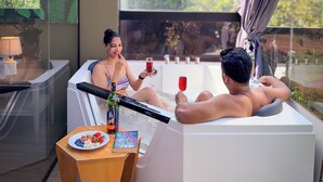 A modern room with a glass-enclosed jacuzzi, a wooden table with snacks and a drink, and a view of greenery outside. - The Blackberry Retreat Kandy (Kandy)