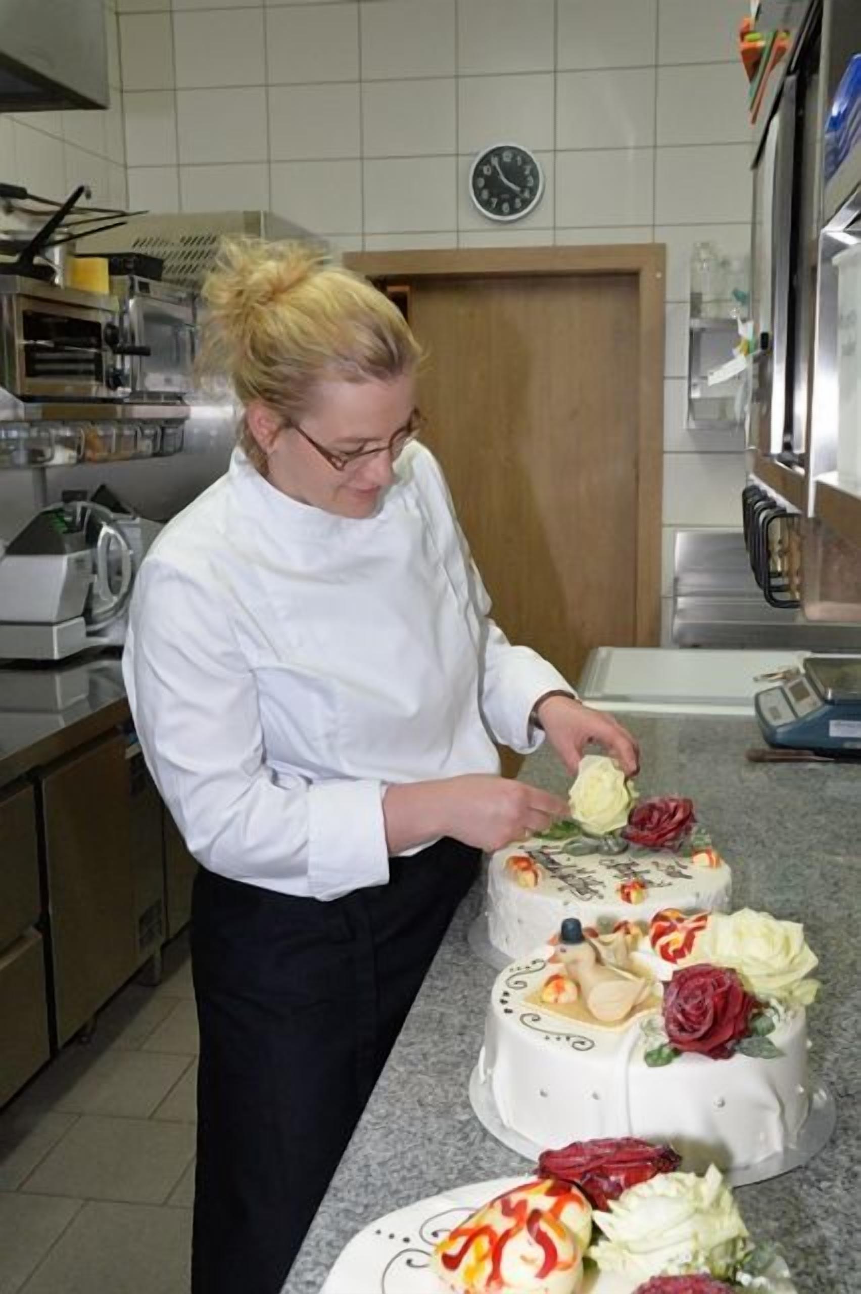 Un chef dans une cuisine où plusieurs gâteaux sont exposés.