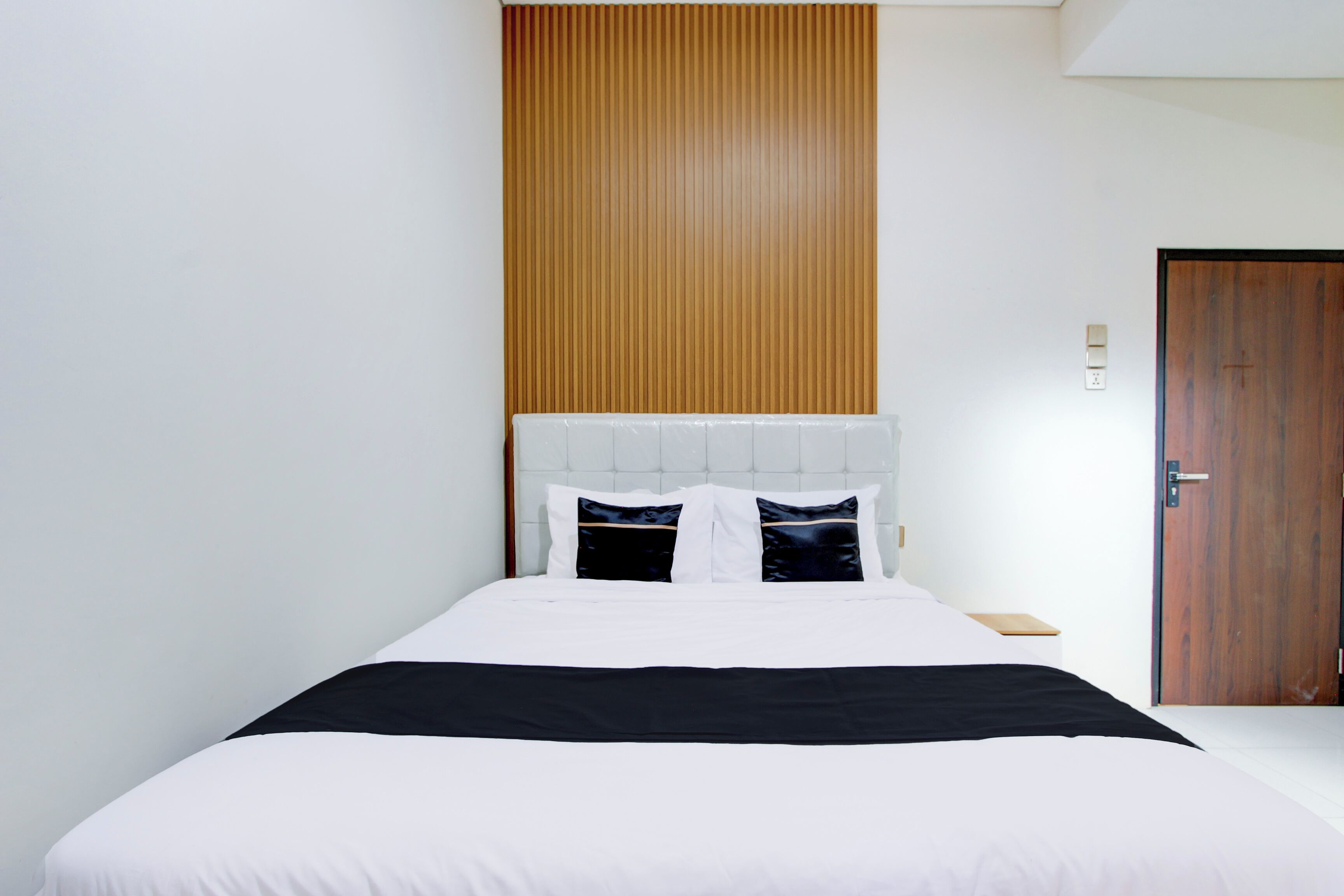 A neatly made bed with white and black bedding, a wooden panel wall, and a wooden door.