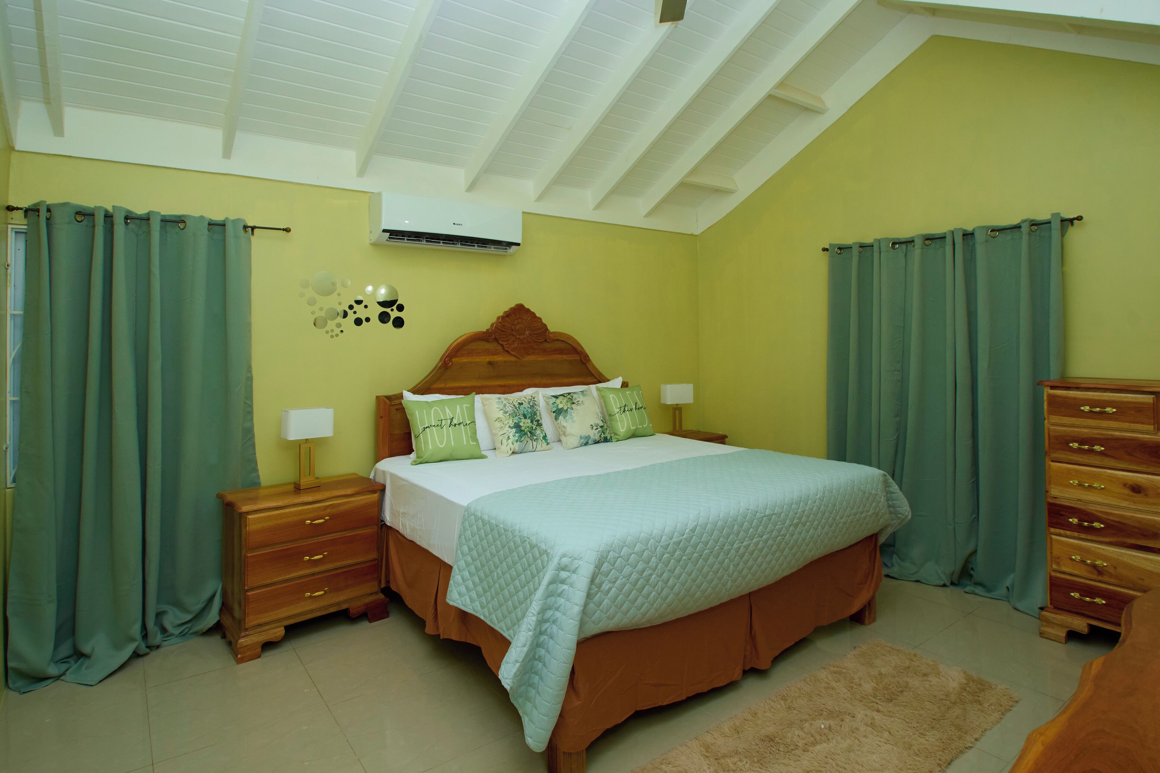 Une chambre à coucher avec un lit, des tables de chevet, une commode et des rideaux verts.