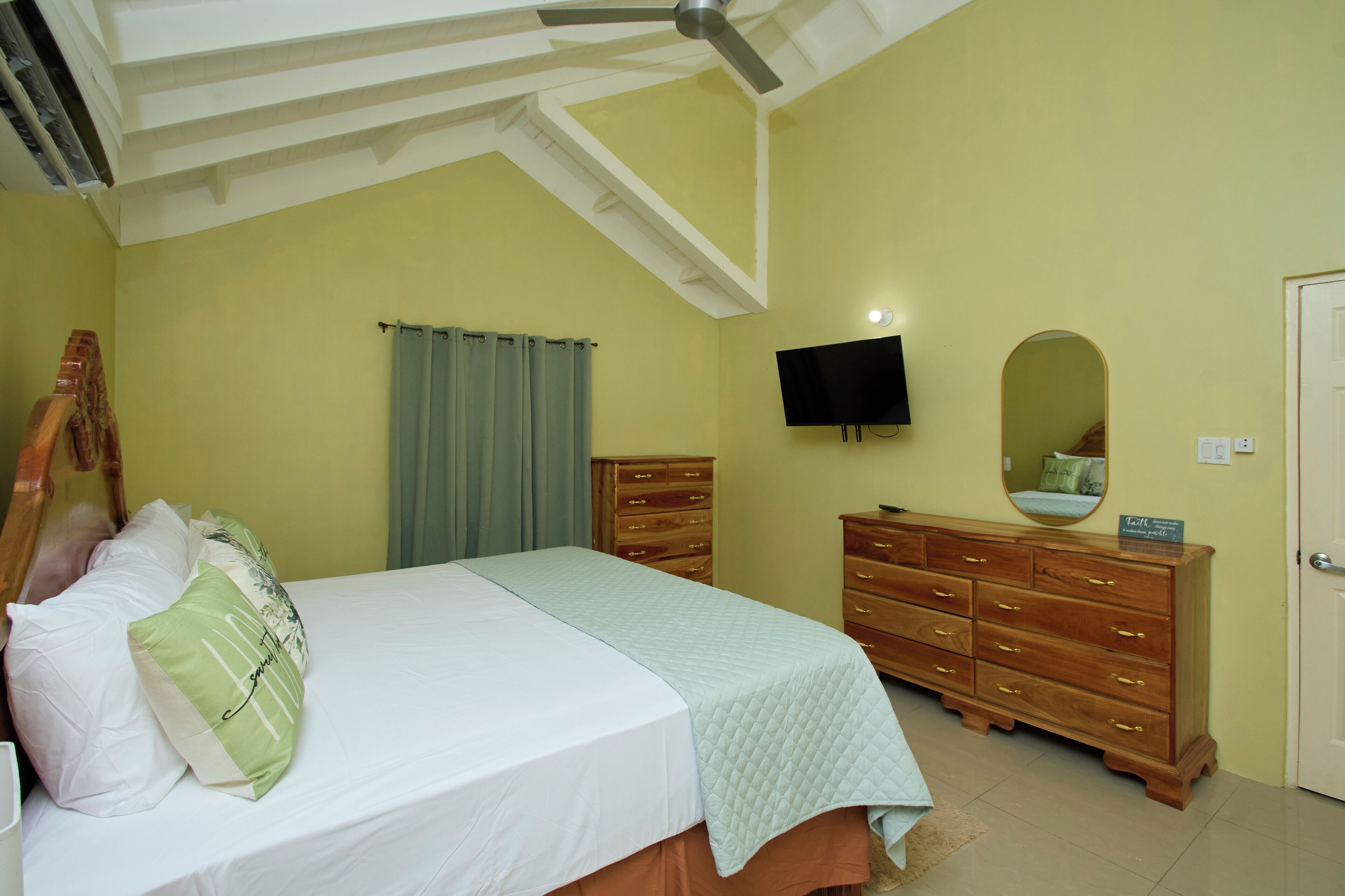 Una camera da letto con un letto, una cassettiera in legno, una TV a schermo piatto, una ventola a soffitto e uno specchio.
