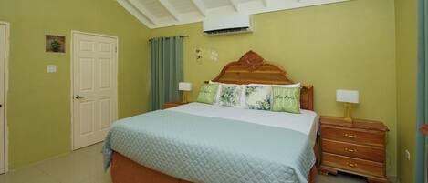 A bedroom with a bed, nightstands, a dresser, a door, and an air conditioning unit.