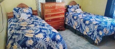 A bedroom with two beds, each with a floral bedspread, a wooden dresser, and a small potted plant on the dresser.