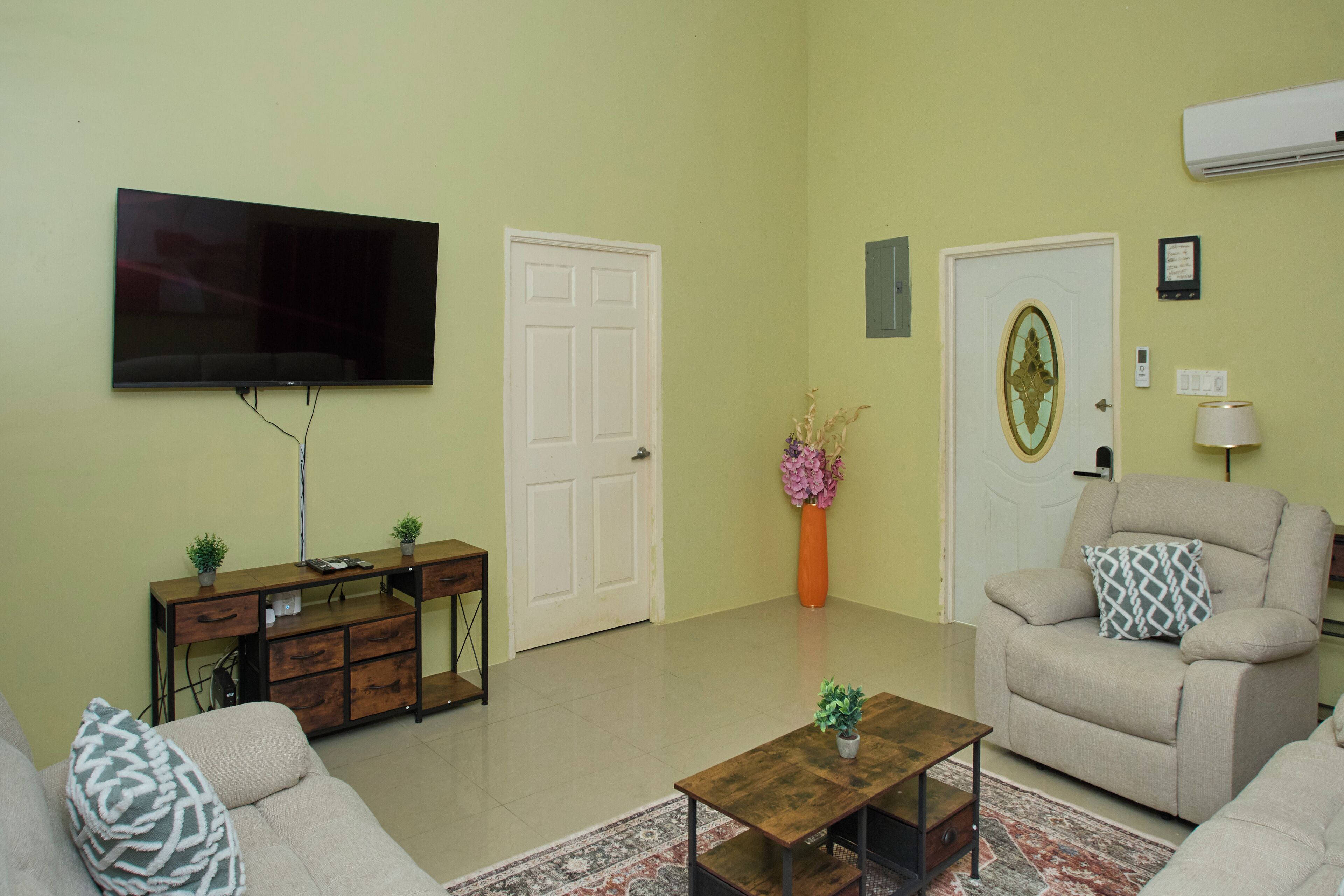 A living room with a flat-screen TV, a sofa, a coffee table, a cabinet, and a door with a decorative glass panel.