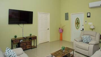 A living room with a flat-screen TV, a sofa, a coffee table, a cabinet, and a door with a decorative glass panel.