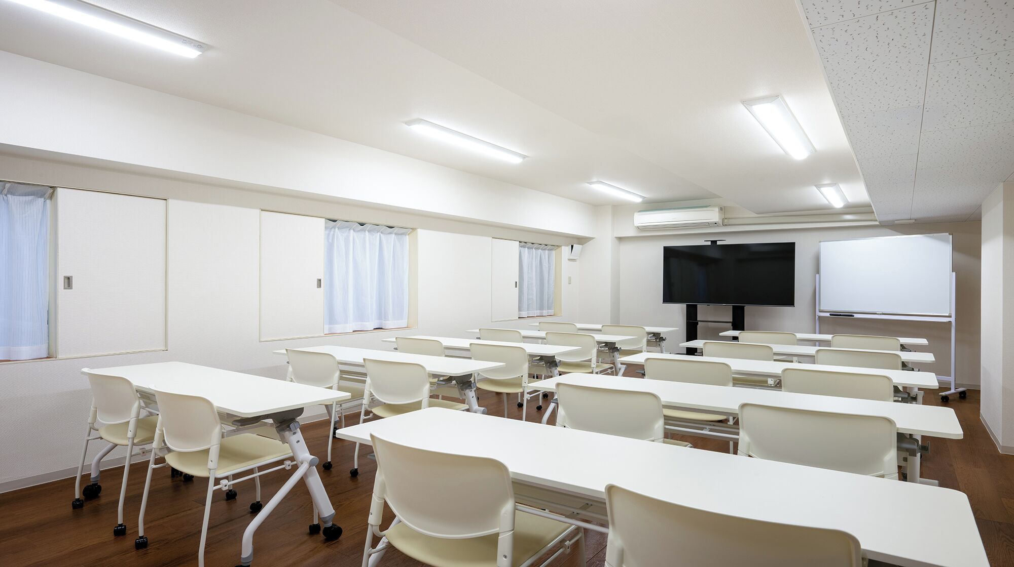 A classroom with white desks and chairs, a large TV screen, and a whiteboard.