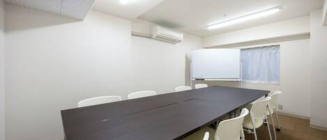 Ein Konferenzraum mit langem Tisch, weißen Stühlen, einer Whiteboard und einer Klimaanlage.