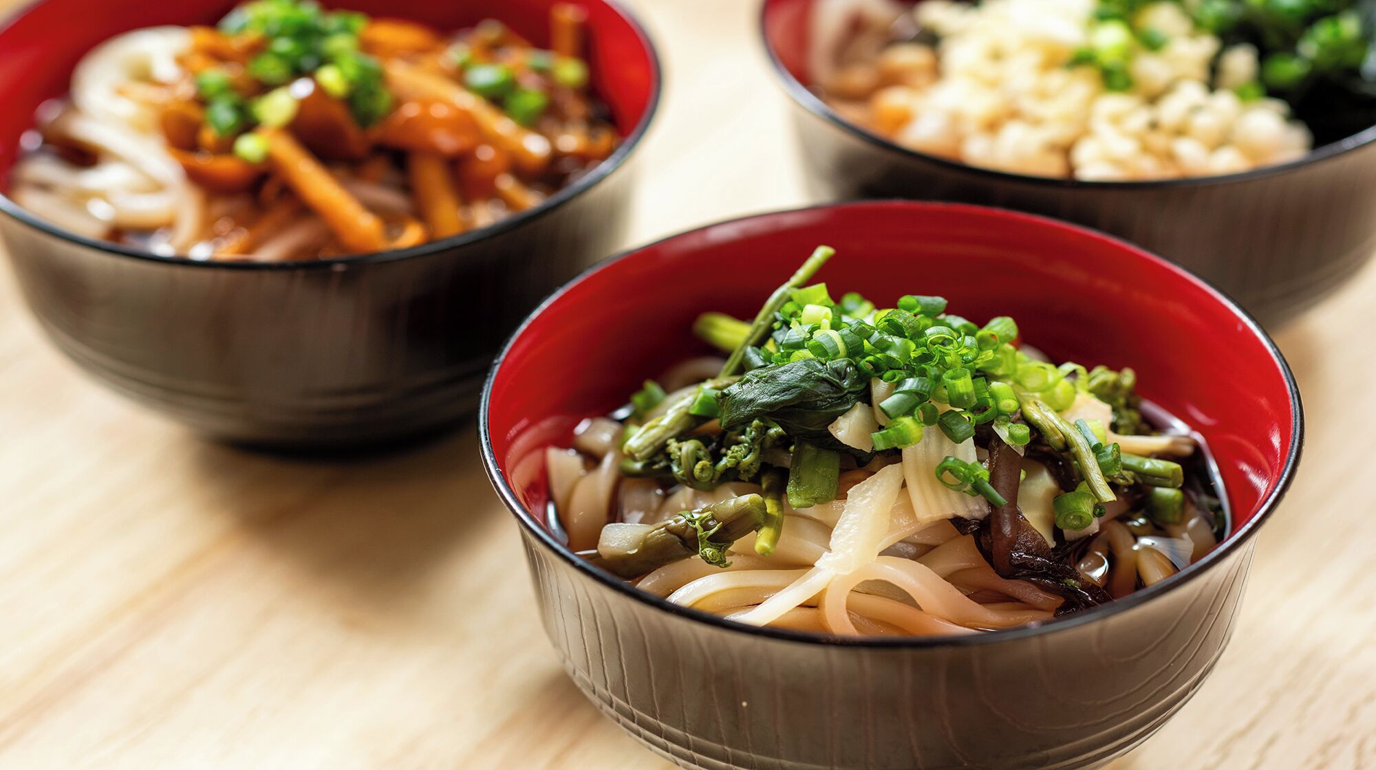 Three bowls of noodle soup with various toppings.