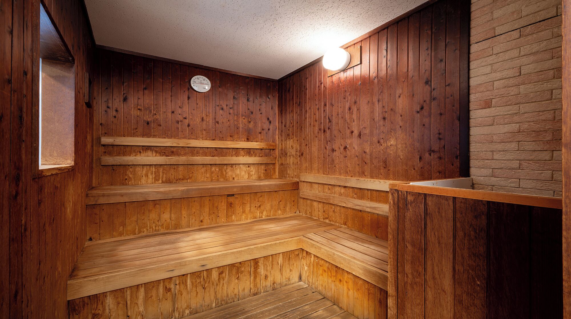 Un sauna avec des bancs en bois et un mur en briques.