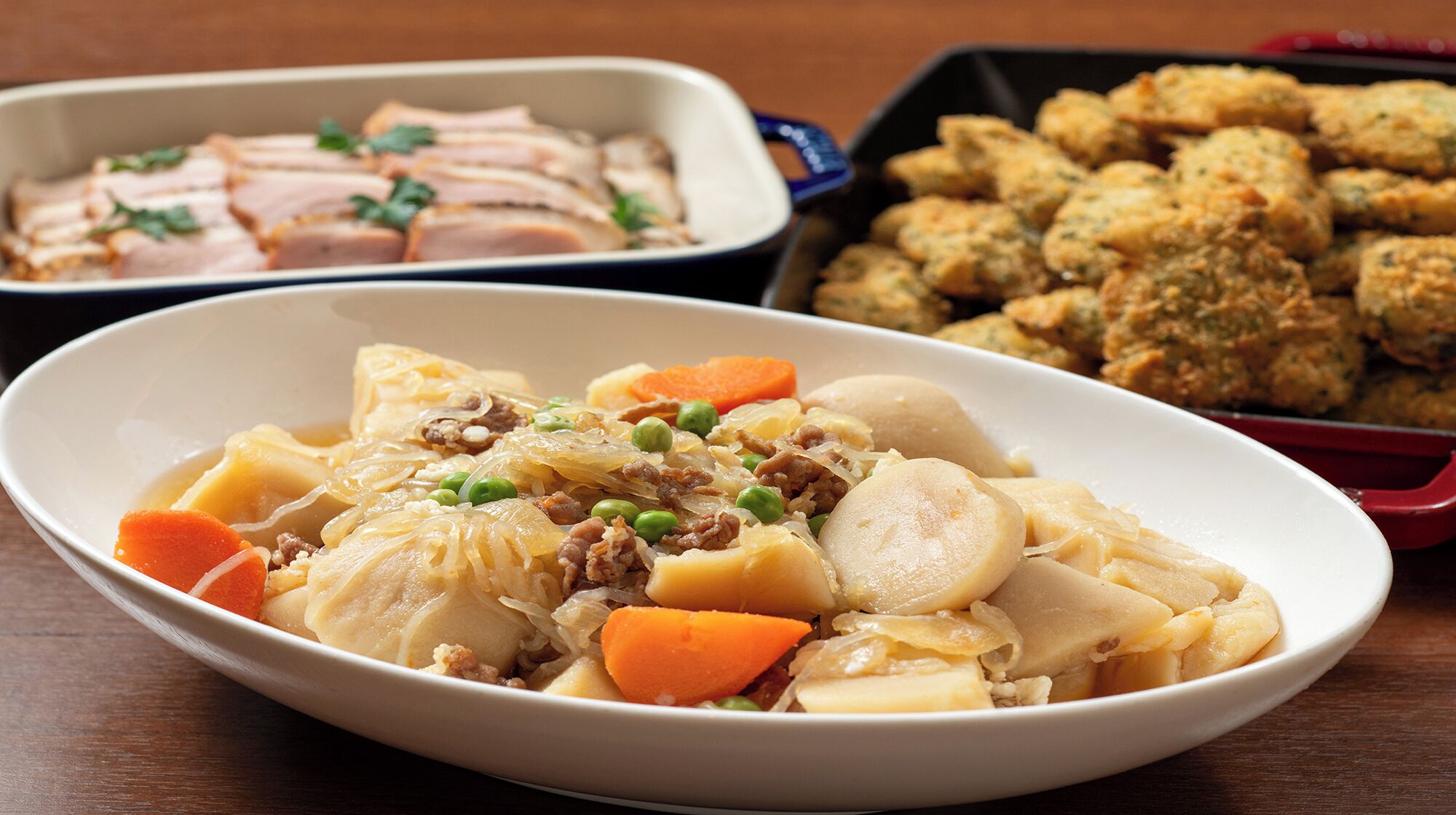 A meal with a variety of dishes including a casserole, a tray of sliced meat, and a plate of breaded items.