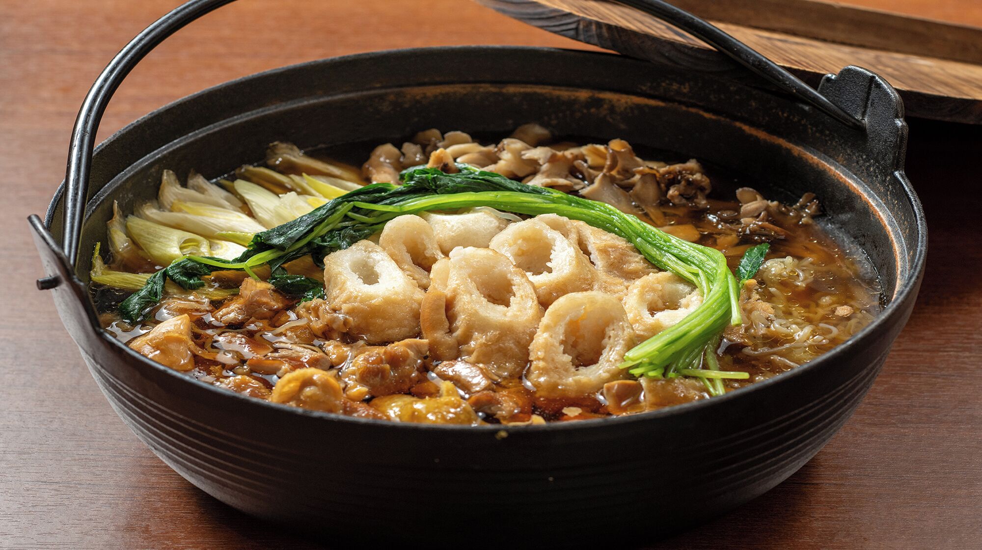 Un tazón de sopa con diversos ingredientes, entre ellos hojas verdes y carne, servido en un tazón negro con asa.