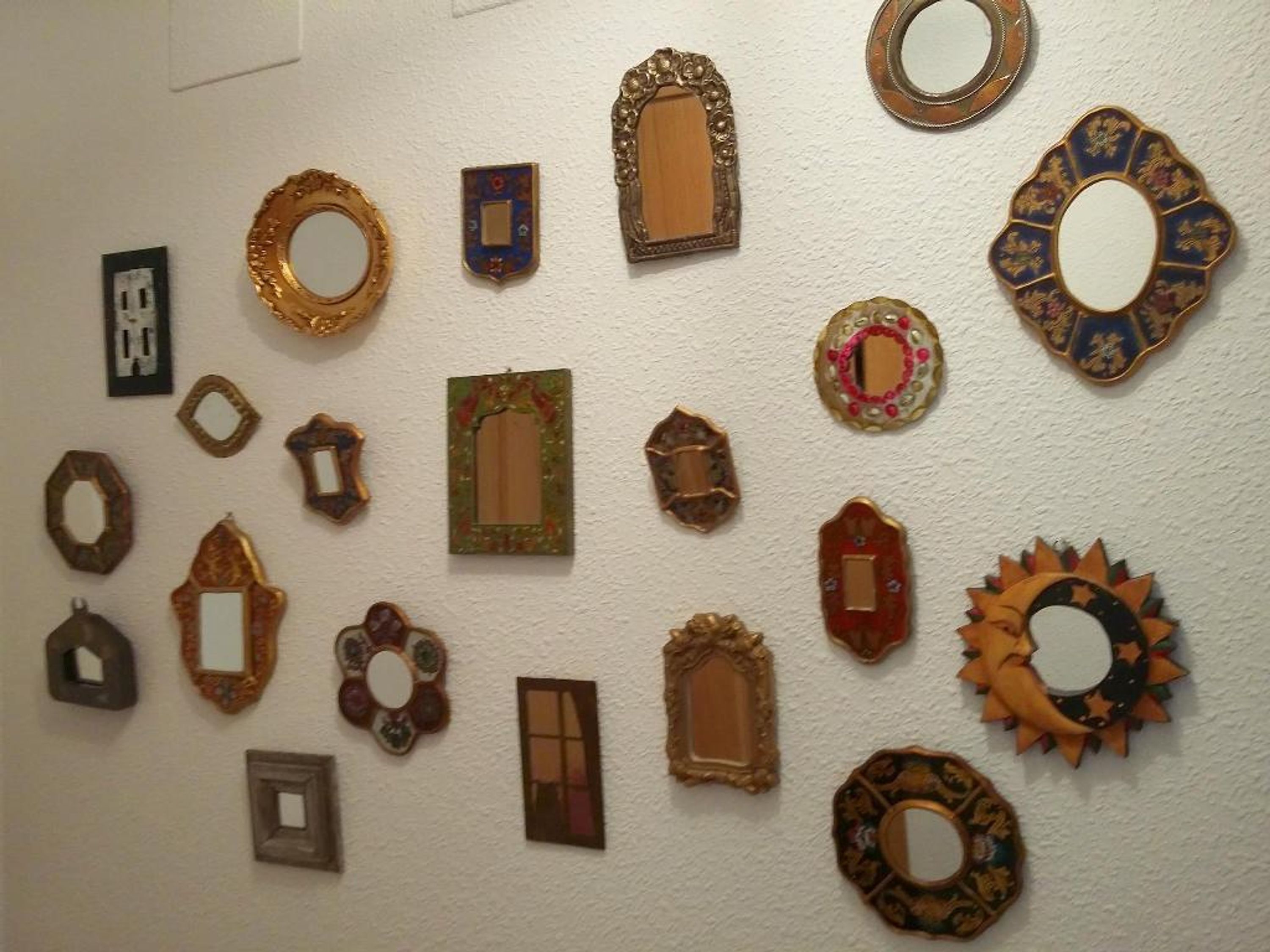A collection of variously shaped and styled mirrors and picture frames on a wall.