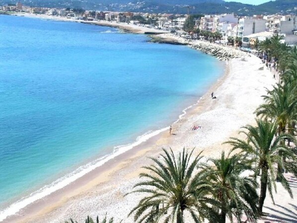 A coastal beach with a sandy shore, palm trees, and buildings in the background. - Apartment- Charly in Javea (Javea)