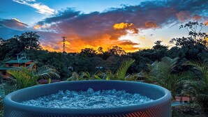 A hot tub surrounded by lush greenery and a sunset with clouds. - Tropical House (La Fortuna)