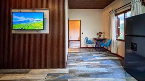 A modern kitchen with a large refrigerator, a wooden accent wall, and a television displaying a scenic landscape. - Tropical House (La Fortuna)