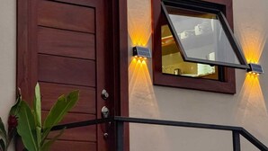 A wooden door with a window above it, both illuminated by wall-mounted lights. - Tropical House (La Fortuna)