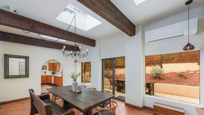 A spacious dining area with a wooden table and chairs, a chandelier, and a view of the outdoors through large windows.