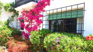 Un edificio con fachada blanca, un balcón con barandillas negras y un ventanal con toldo verde.