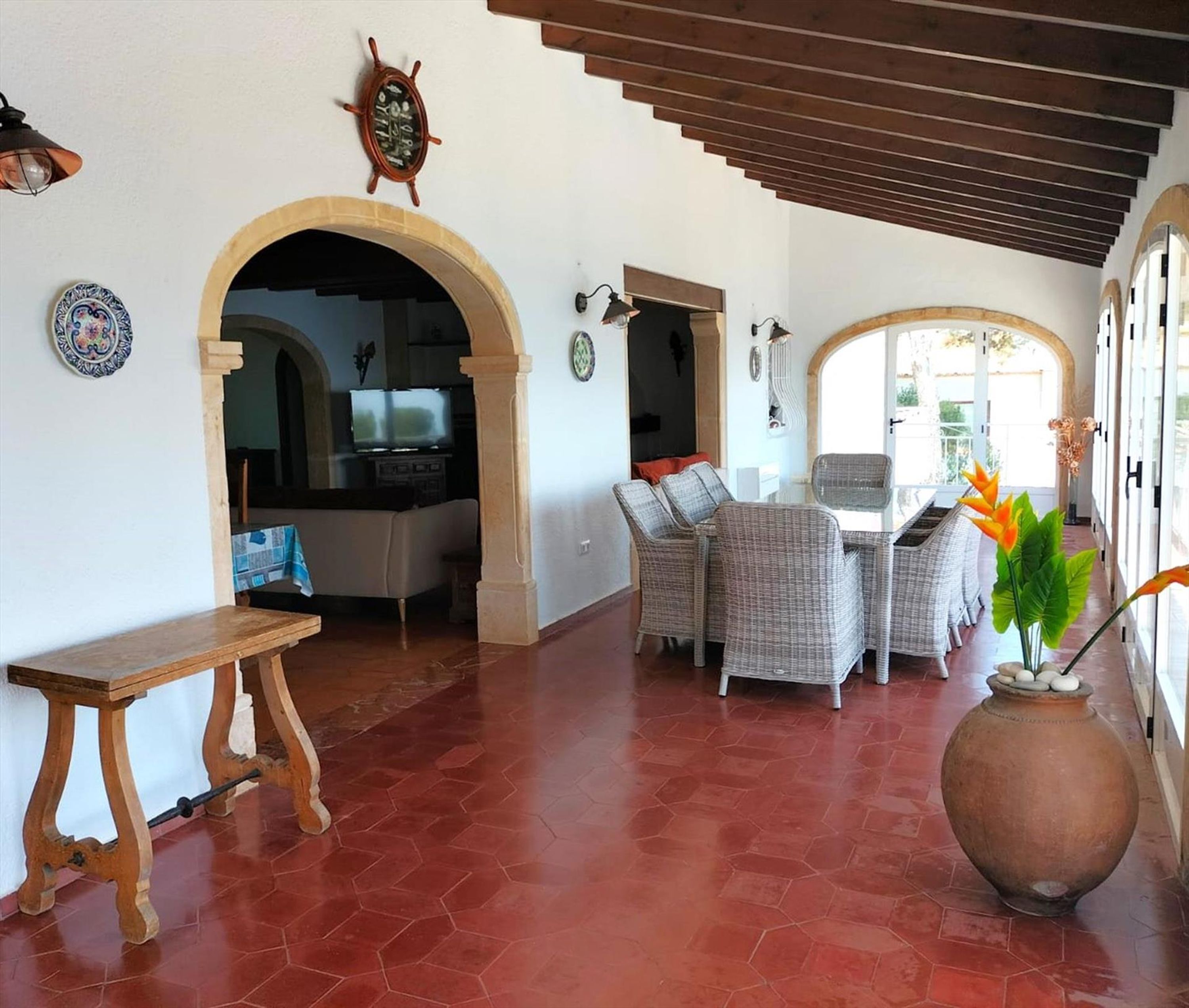 Amplia sala de estar con comedor, un jarrón grande con flores y un televisor al fondo.