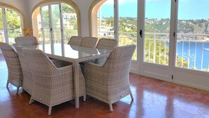 A dining area with a glass table and wicker chairs, large arched windows with a view of the sea and buildings. - Maria 10 in J vea With 5 Bedrooms and 3 Bathrooms (Javea)