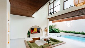 Un amplio espacio interior con piscina, una chimenea y una zona de estar con cojines verdes.