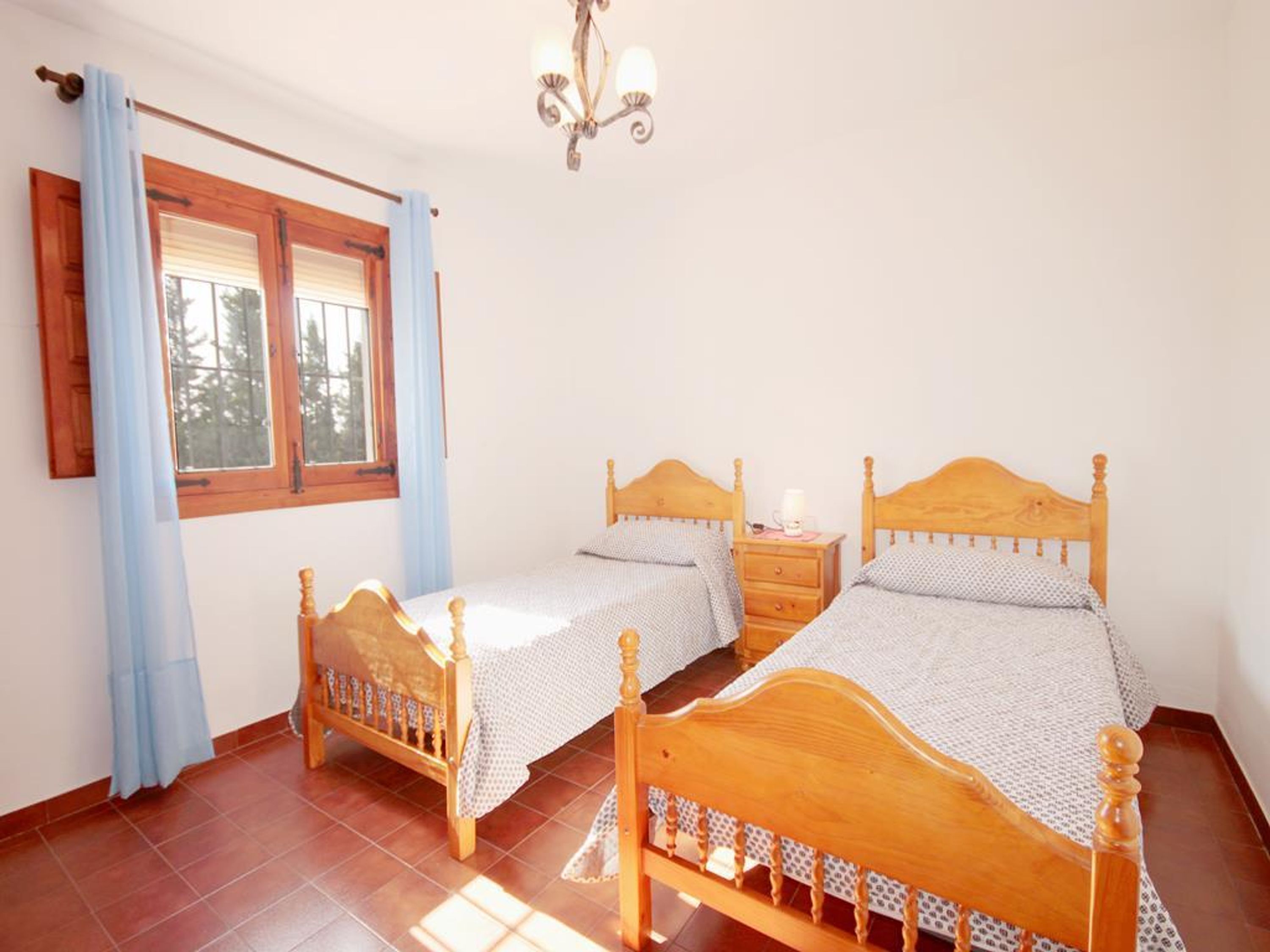 A bedroom with two wooden beds, a window with curtains, and a chandelier.