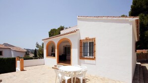 A white building with arched doorways and a tiled roof. There is a patio with a table and chairs. - Villa- Caleta in Portichol (Javea)