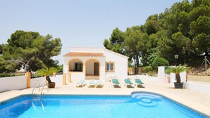 A poolside area with a small building, lounge chairs, and a clear blue pool. - Villa- Caleta in Portichol (Javea)