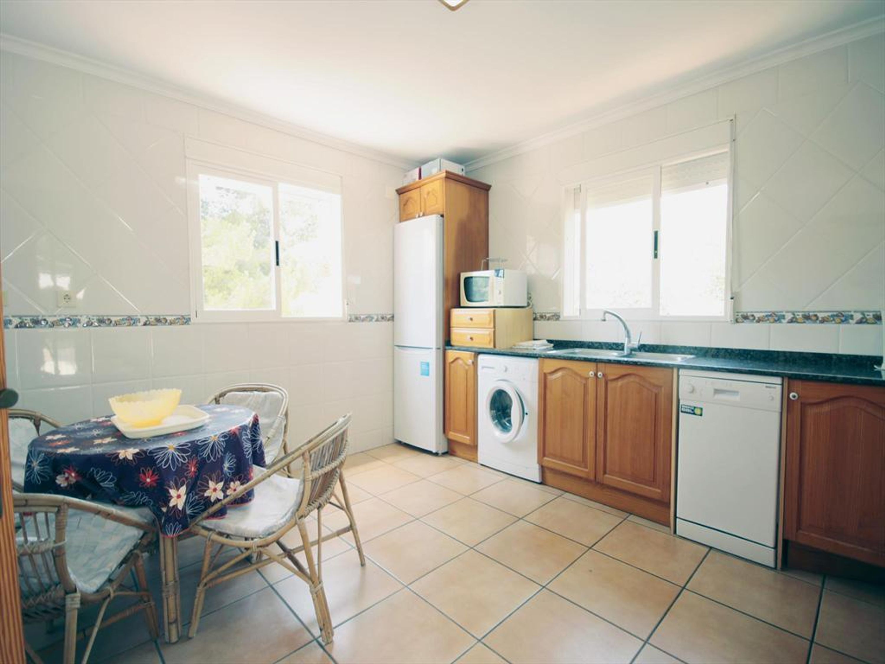 A compact kitchen with a dining table, chairs, a washing machine, a microwave, and a dishwasher.
