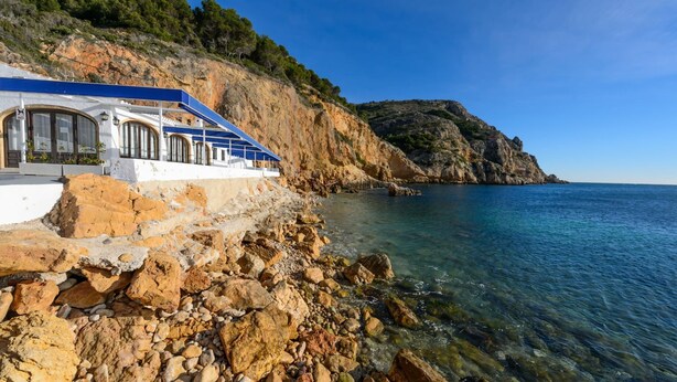 A coastal building with a blue roof, white walls, and large windows. - Villa- Caleta in Portichol (Javea)
