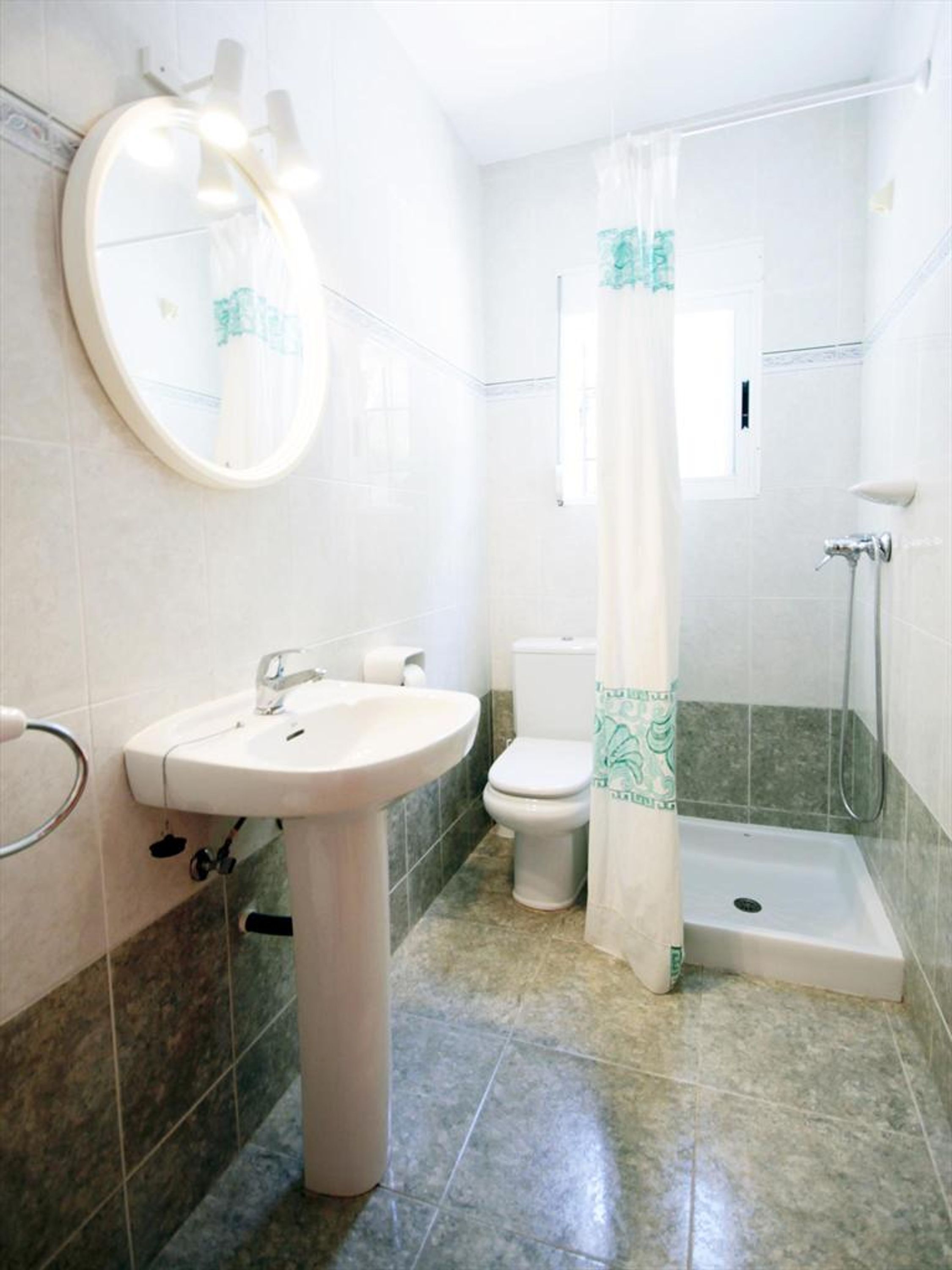 A bathroom with a sink, toilet, shower, and a mirror with lights.