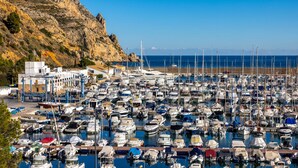 Ein Yachthafen voller Boote, die an der Mole liegen, mit einer felsigen Klippe im Hintergrund und einem strahlend blauen Himmel.