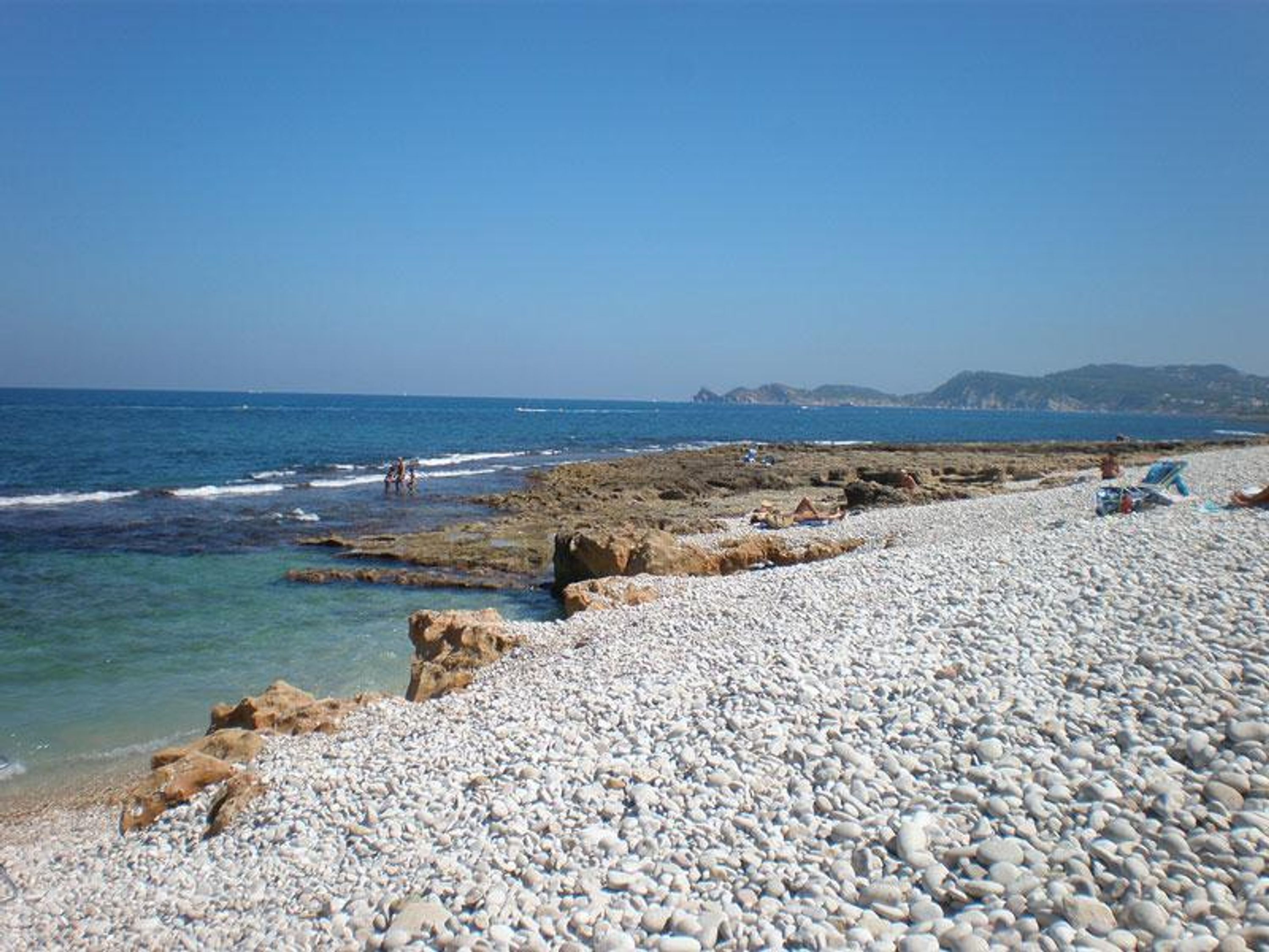 Una spiaggia con ciottoli, affioramenti rocciosi e mare calmo.