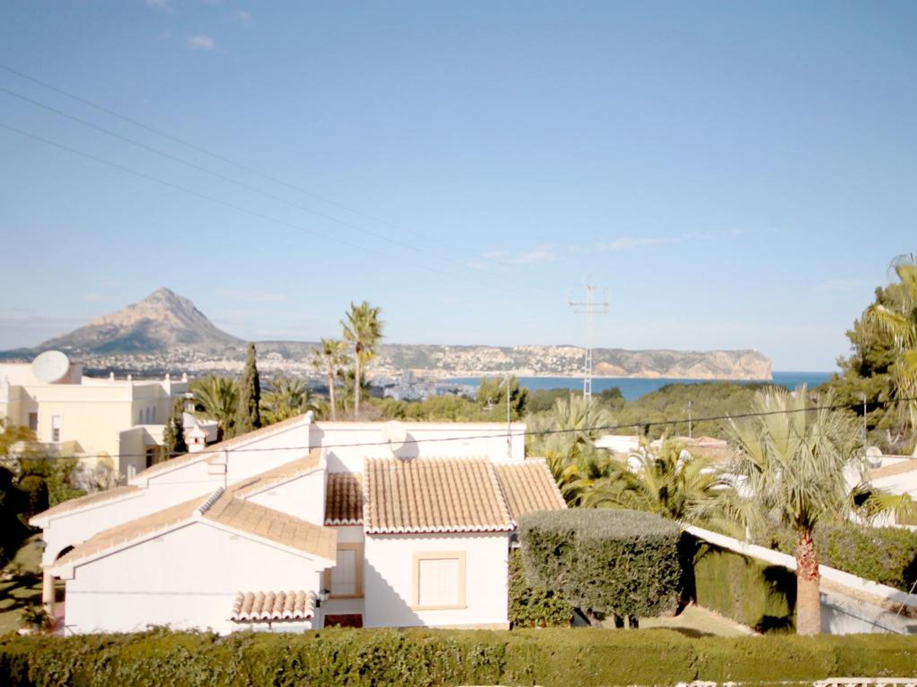 Quartiere residenziale con un edificio bianco, una montagna sullo sfondo e un cielo azzurro limpido.