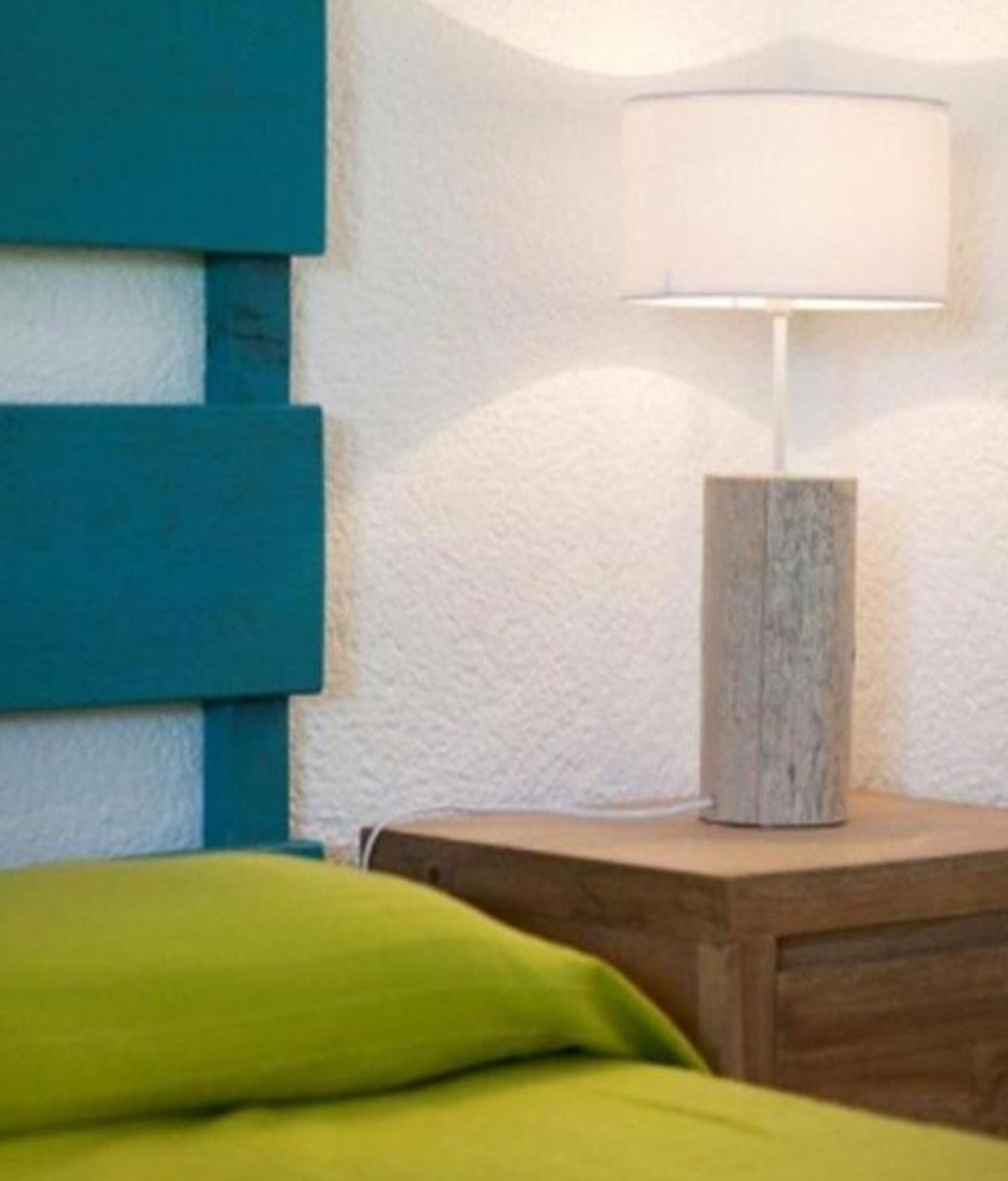 A room with a bed, a nightstand, a lamp, and a wall with a textured finish.