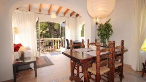 Un espace repas comprenant une table et des chaises en bois, un luminaire suspendu et une vue sur la terrasse extérieure.